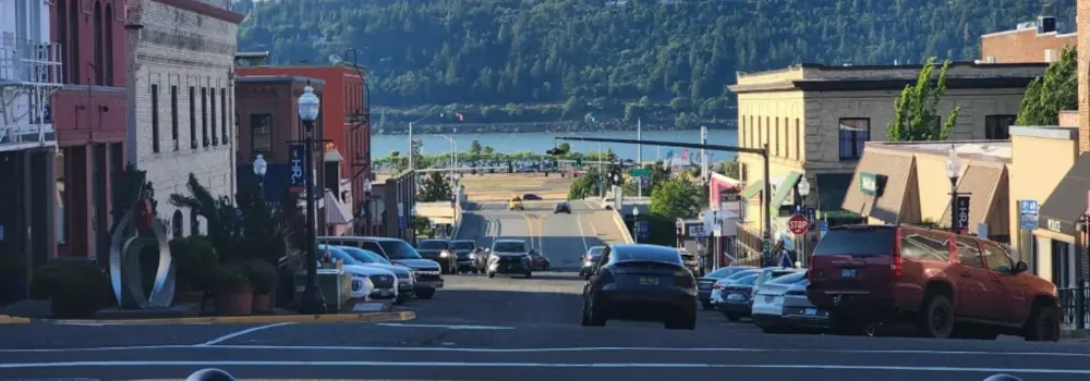 Downtown street descending toward a river and forested hillside.
