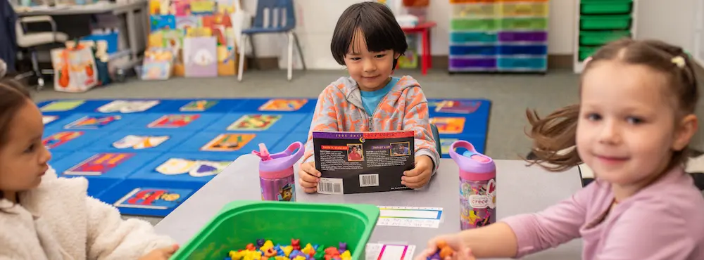 Three young children doing activities at a classroom table.