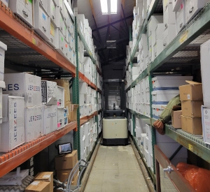 Warehouse aisle with stocked shelves and a pallet jack.