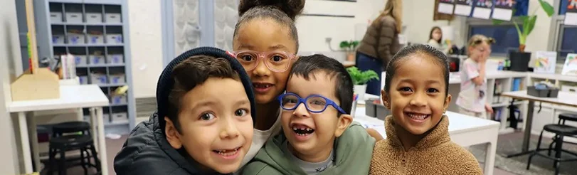 Four smiling children posing together in a classroom.