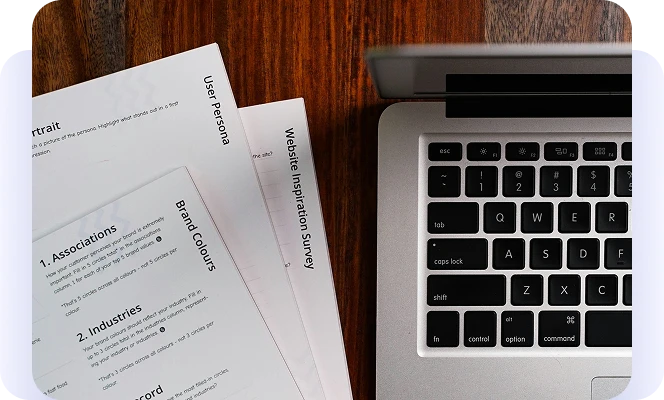 Brand strategy survey documents beside a laptop on a wooden desk.